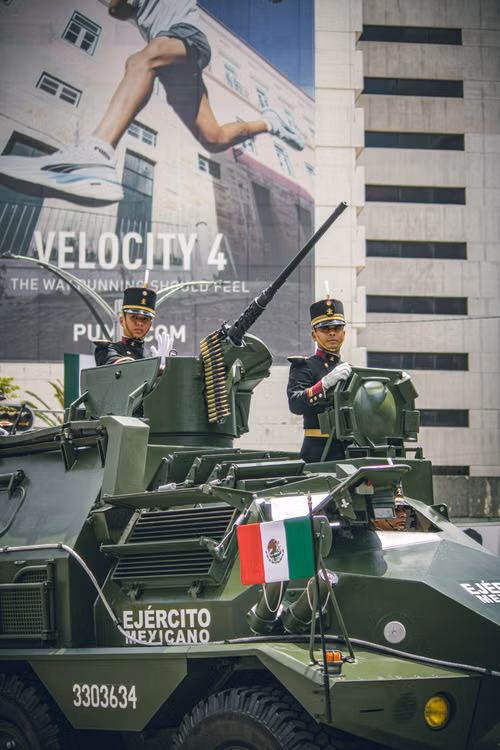 Ilustración de militares desfilando con una bandera mexicana frente a edificios; no representa una edición específica.